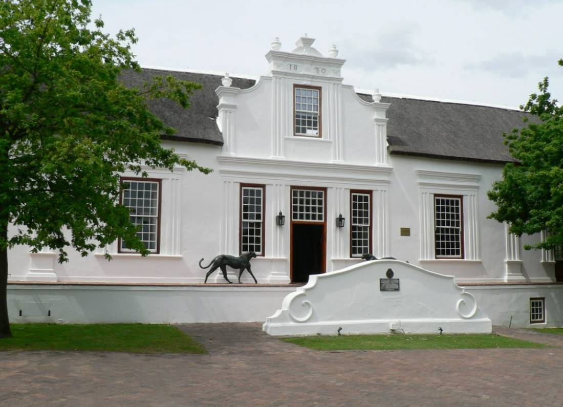 A white Cape Dutch manor house with a curved gable on a green lawn