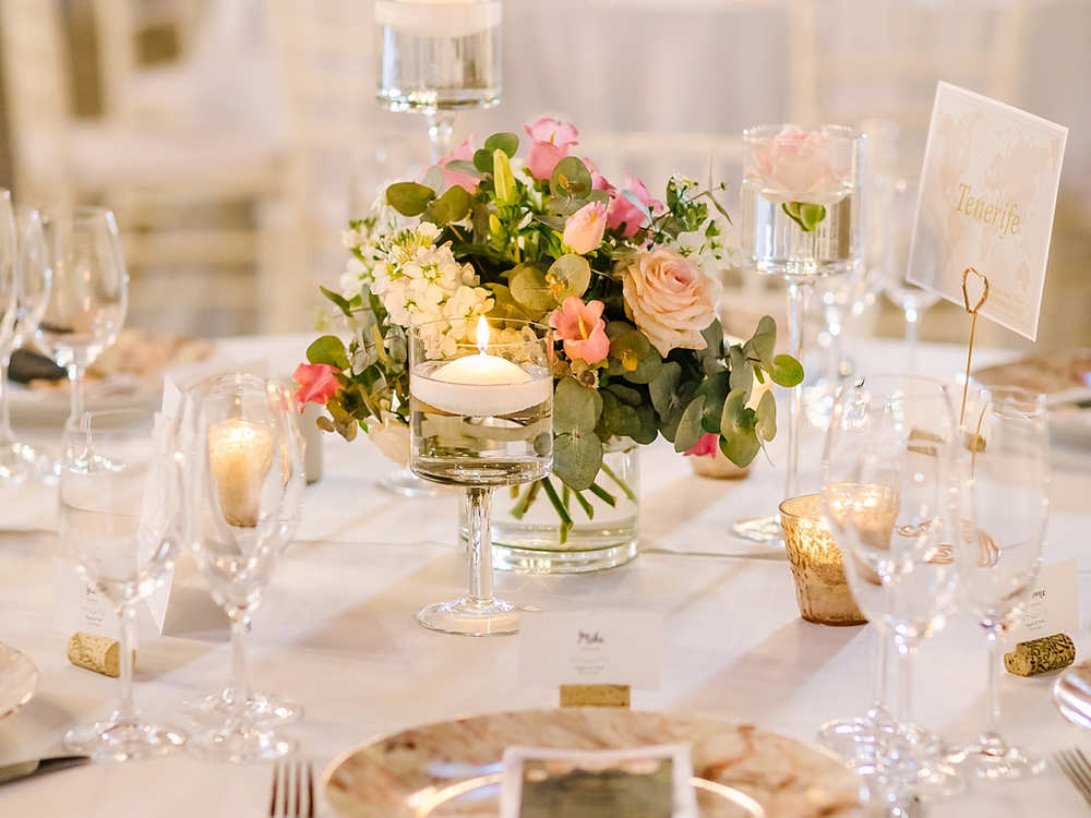 A long table laid with white linen, glasses, candles and pink roses